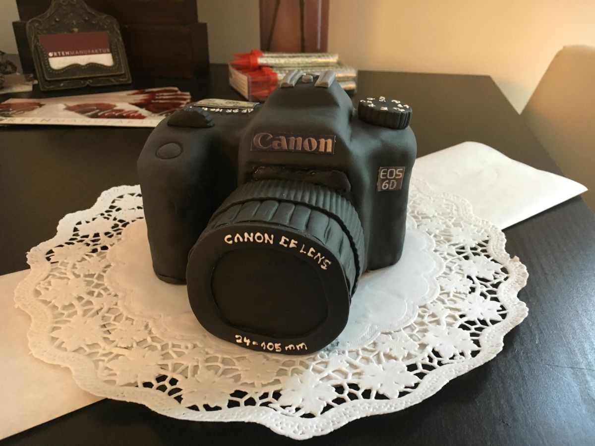 Black Canon camera cake with zoom lens on white lace doily