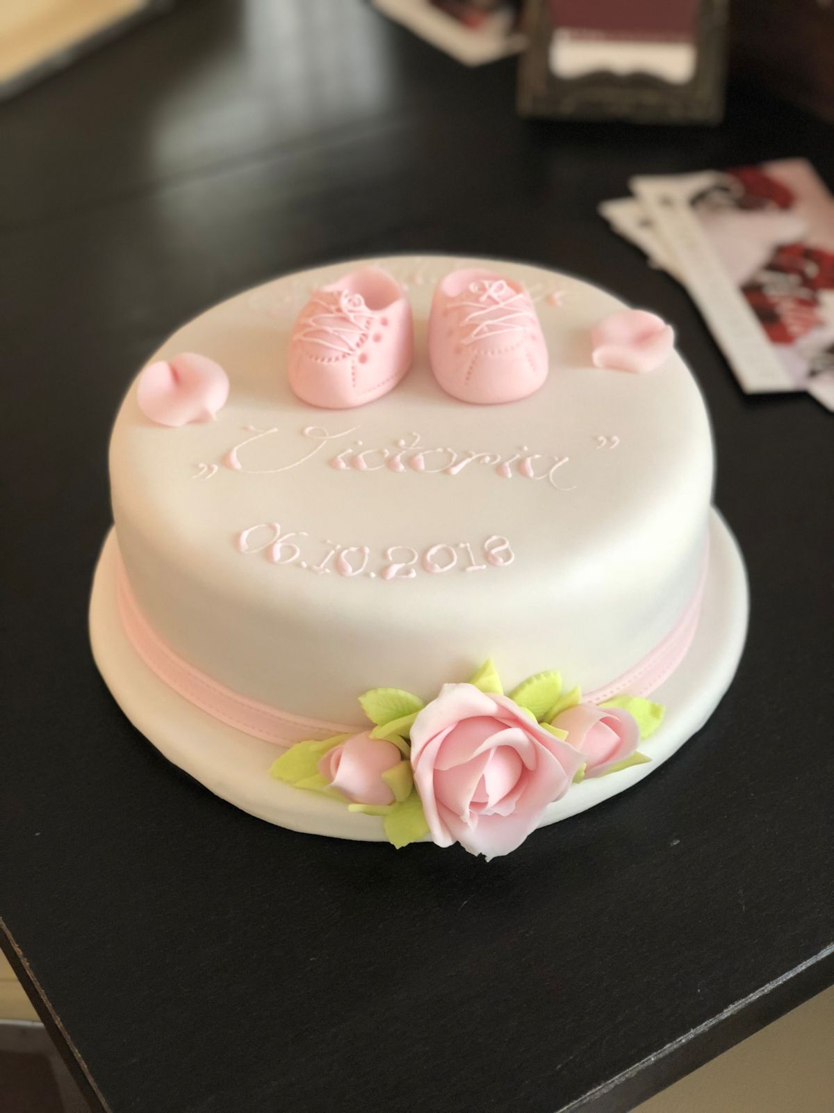 Christening cake with pink baby shoes in the centre and fresh roses