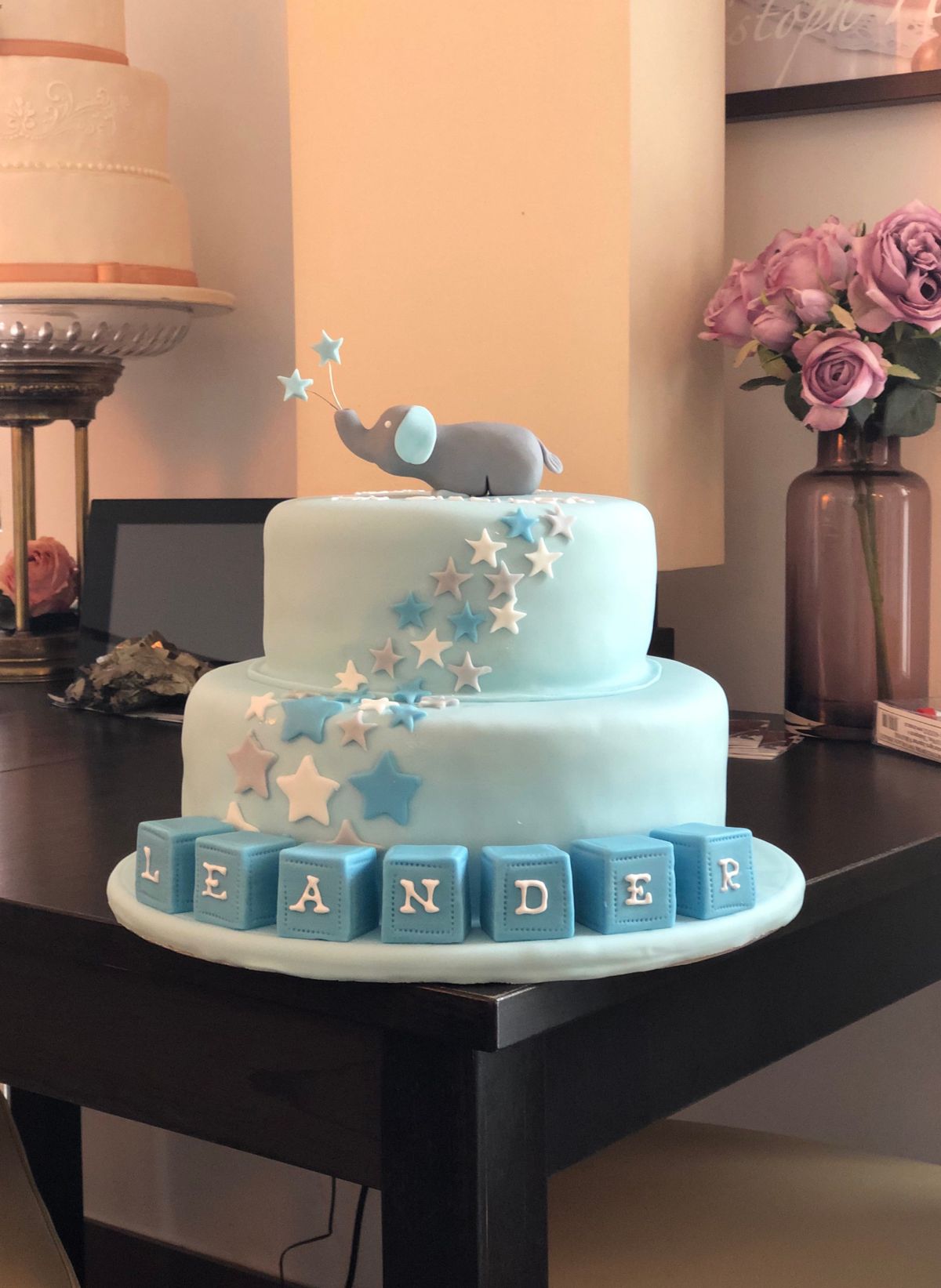 Two-tier light blue christening cake with elephant figurine and stars